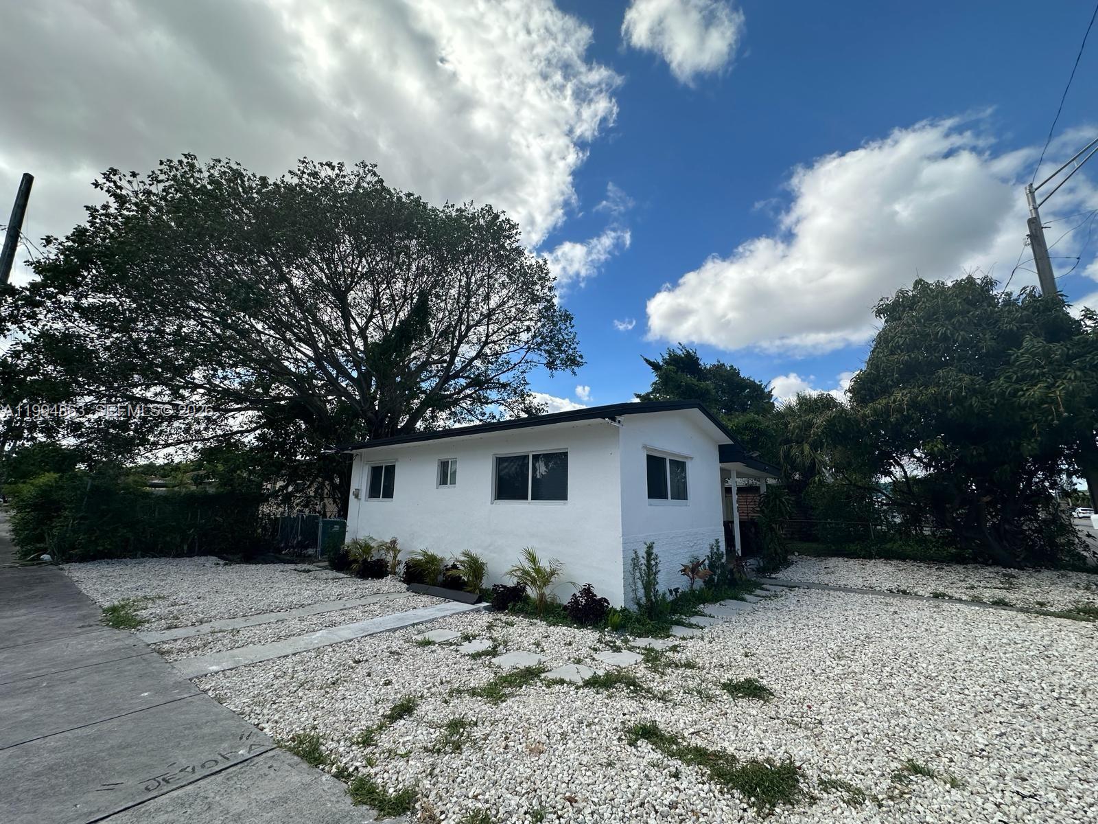 A white, single-story house with a gravel yard and a large tree in the background — 7460 NW 17th Ave, Miami FL 33147, MIAMI, FL