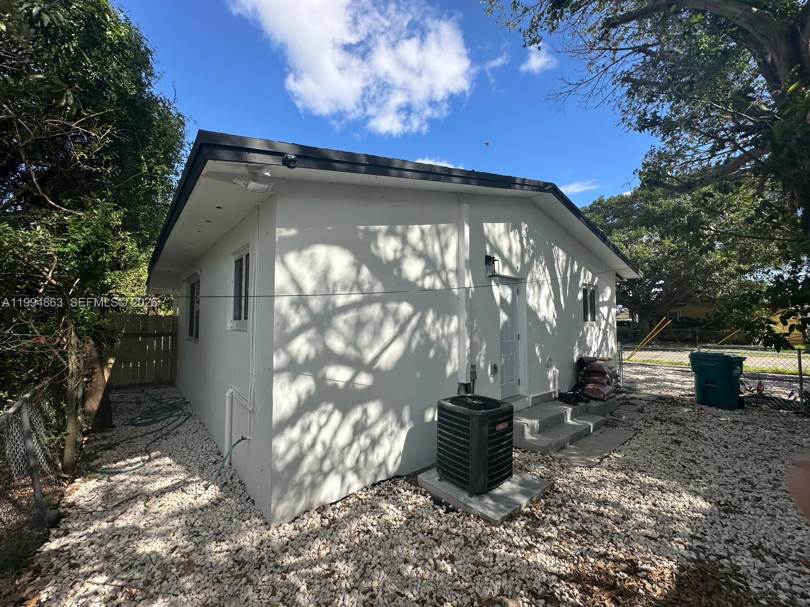 The exterior of a white, single-story house features a gravel yard and an air conditioning unit — 7460 NW 17th Ave, Miami FL 33147, MIAMI, FL