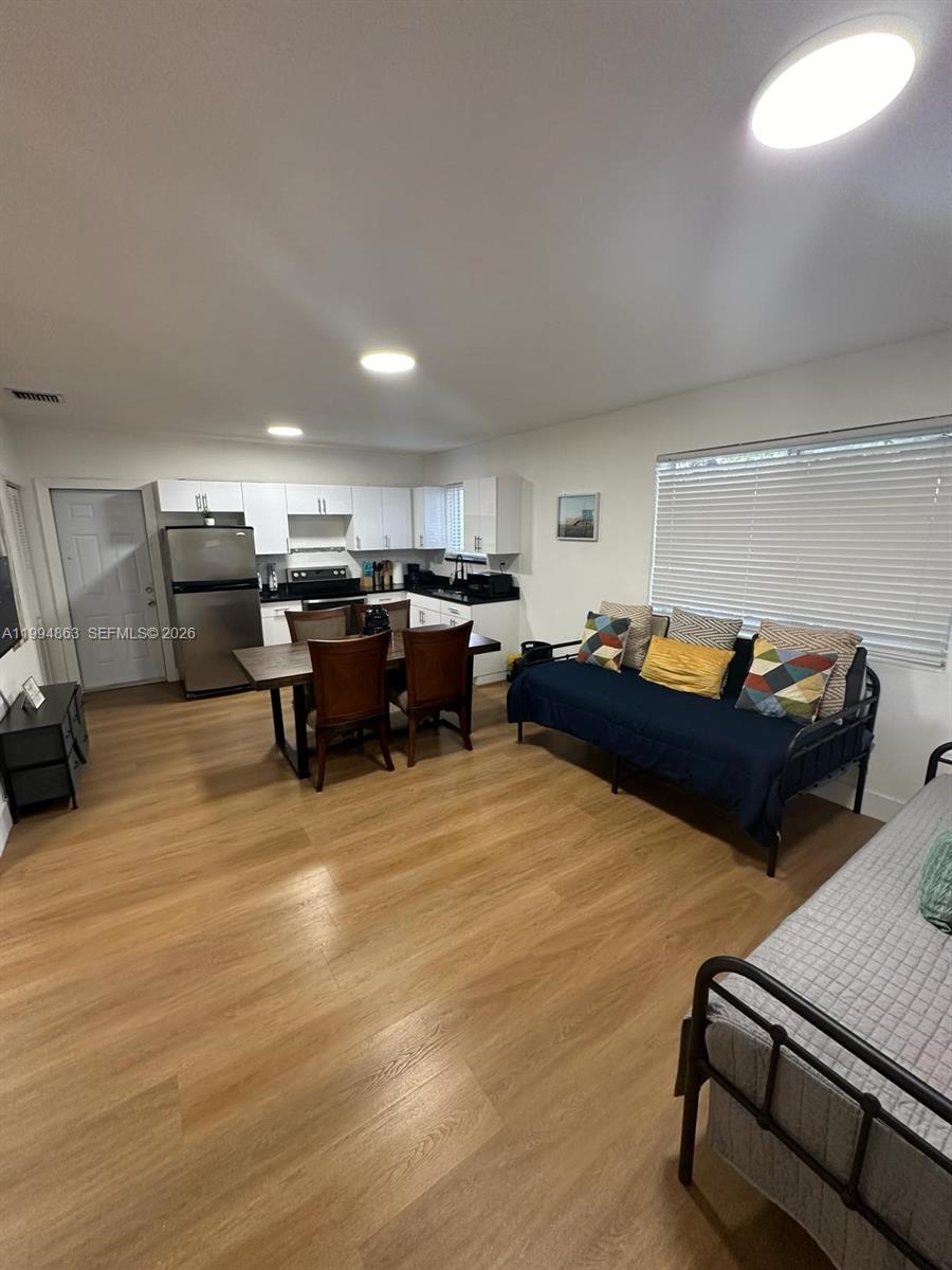 This open-concept living area features a kitchen, dining table, and daybeds on wood flooring — 7460 NW 17th Ave, Miami FL 33147, MIAMI, FL