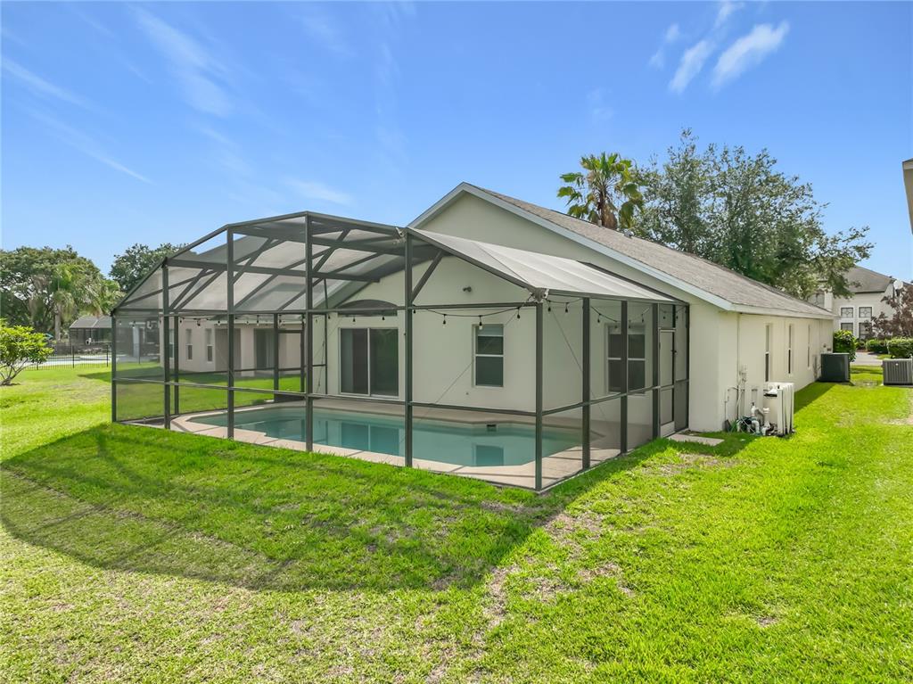 A backyard view of a house with a screened-in pool enclosure and a grassy lawn — 5373 TORTUGA DRIVE, ORLANDO, FL