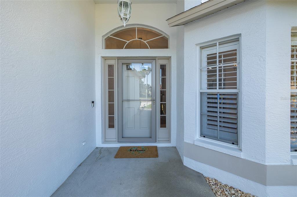 A front entryway with a light-colored door, sidelights, an arched transom window, and a welcome mat — 11428 HIDDEN COVE COURT, TRINITY, FL