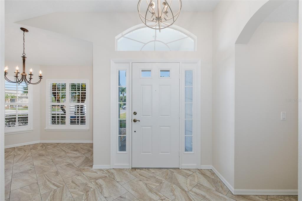 A bright entryway features a white front door with sidelights, tile flooring, and two chandeliers — 11428 HIDDEN COVE COURT, TRINITY, FL