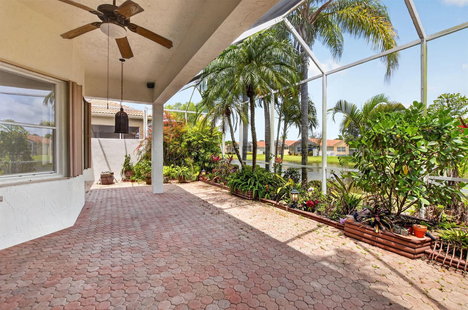 A covered patio with brick pavers, a ceiling fan, and a screened-in view of a pond — 7035 Vivaldi Lane, Delray Beach FL 33446, DELRAY BEACH, FL