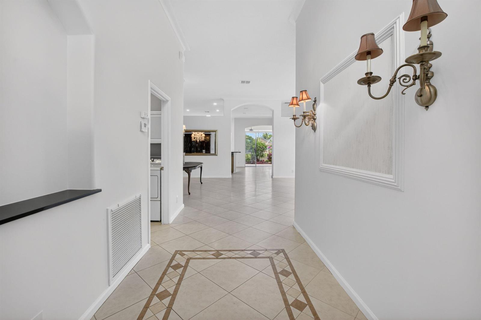 A bright hallway with tiled floors leads to an open living area with glass doors — 7035 Vivaldi Lane, Delray Beach FL 33446, DELRAY BEACH, FL
