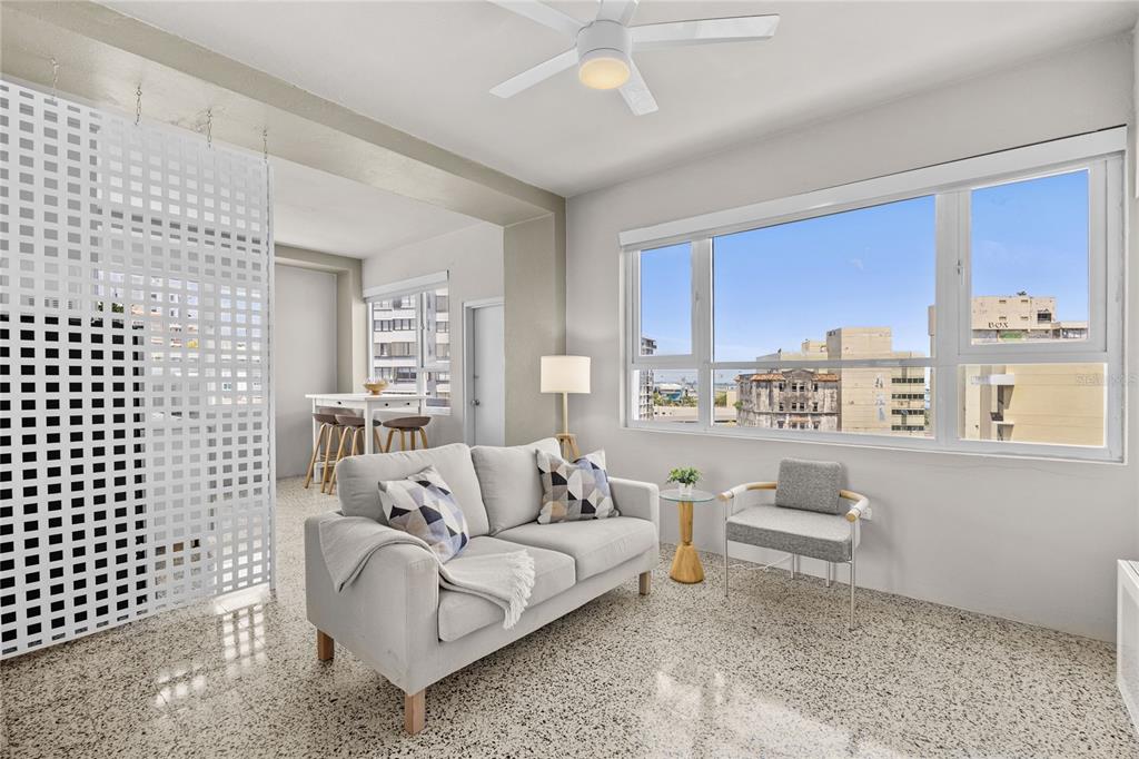 A living room with a light gray sofa, a patterned chair, and large windows overlooking buildings — 603 MIRAMAR AVENUE UNIT 7, SAN JUAN, PR