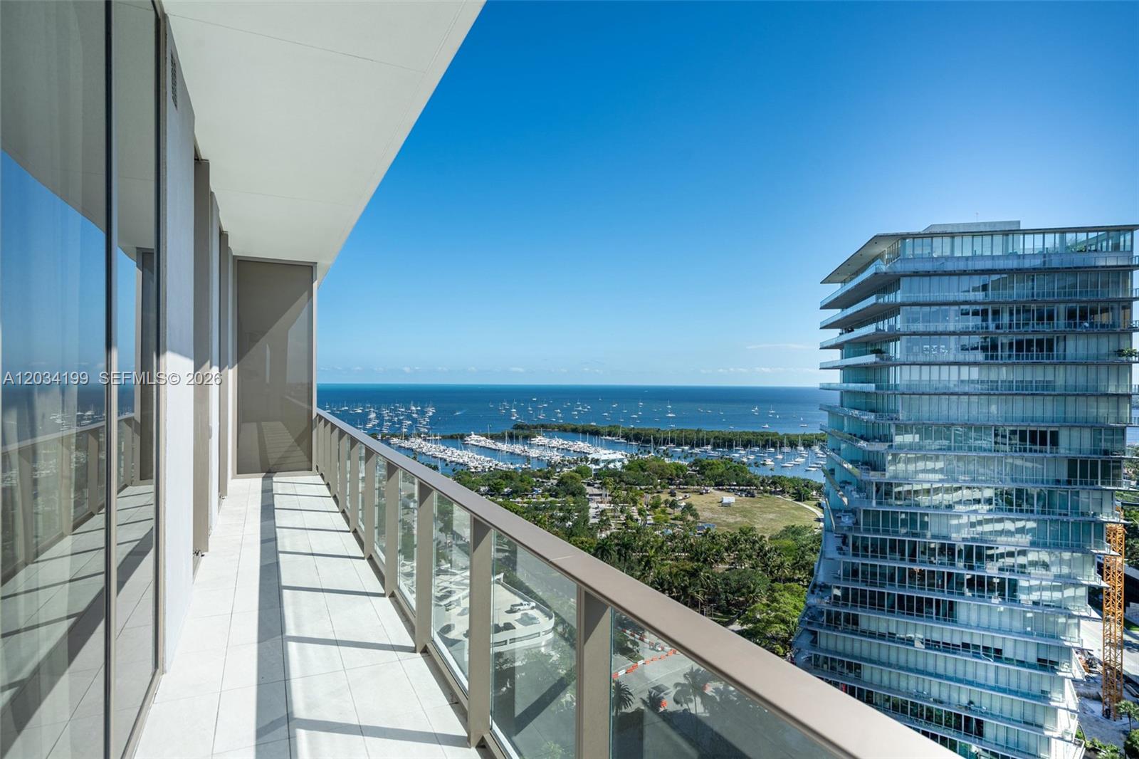 A balcony with glass railings overlooks a marina, a park, and a neighboring high-rise building — 2655 S Bayshore Dr # 1911, Miami FL 33133, MIAMI, FL