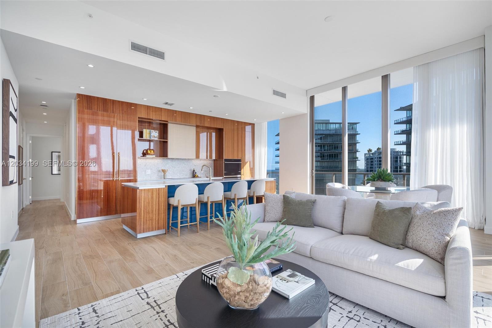 A modern open-concept living room and kitchen with wood cabinetry and floor-to-ceiling windows — 2655 S Bayshore Dr # 1911, Miami FL 33133, MIAMI, FL
