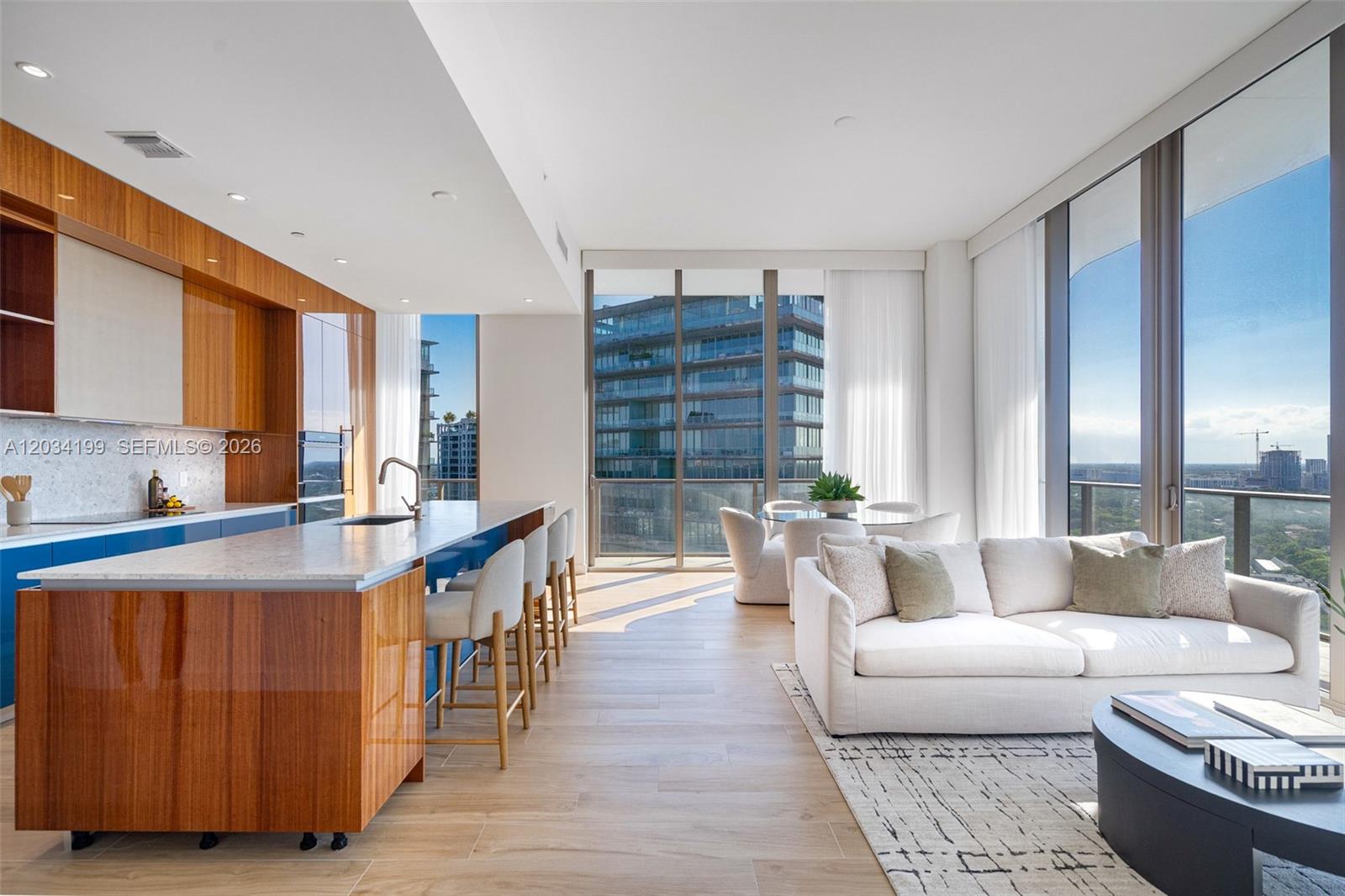 A modern open-concept kitchen and living area with wood cabinetry, a stone island, and floor-to-ceiling windows — 2655 S Bayshore Dr # 1911, Miami FL 33133, MIAMI, FL