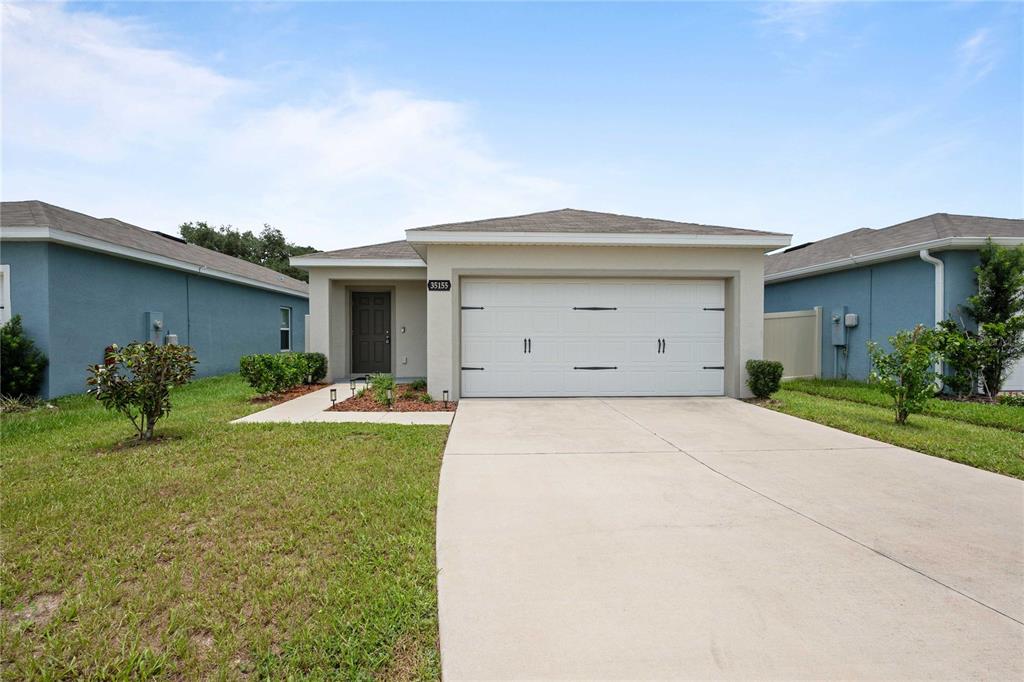 A single-story house with a white garage door, beige stucco exterior, and a concrete driveway — 35155 JOMAR AVENUE, ZEPHYRHILLS, FL