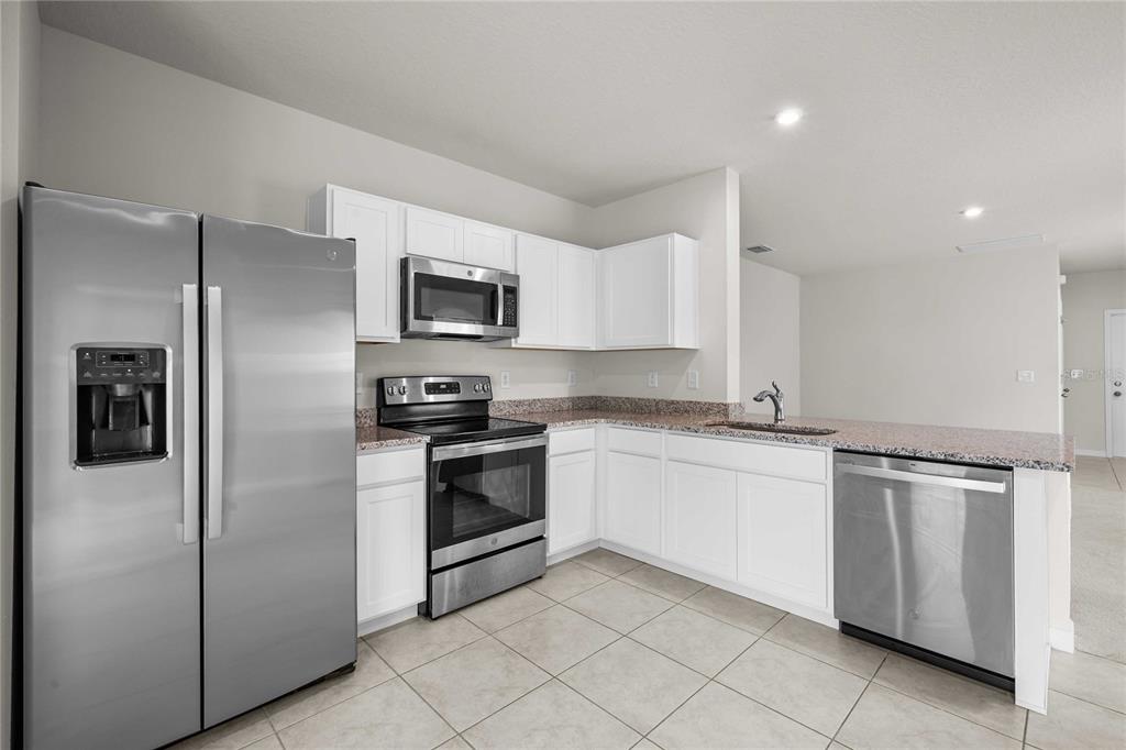A kitchen features white cabinets, stainless steel appliances, granite countertops, and light-colored tile flooring — 35155 JOMAR AVENUE, ZEPHYRHILLS, FL