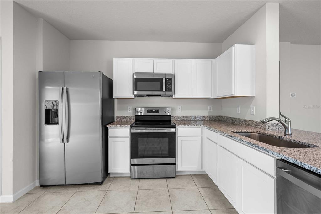 A kitchen features white cabinets, stainless steel appliances, and granite countertops over tile flooring — 35155 JOMAR AVENUE, ZEPHYRHILLS, FL