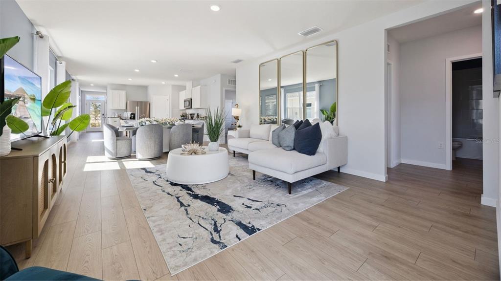 A bright living room features light wood flooring, a white sectional sofa, and three mirrors — 3056 HOUSE FINCH ROAD, ST CLOUD, FL