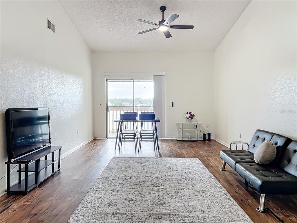 A living room with wood-look flooring, a black sofa, a television, and a dining area — 4166 PLANTATION COVE DRIVE UNIT 505, ORLANDO, FL
