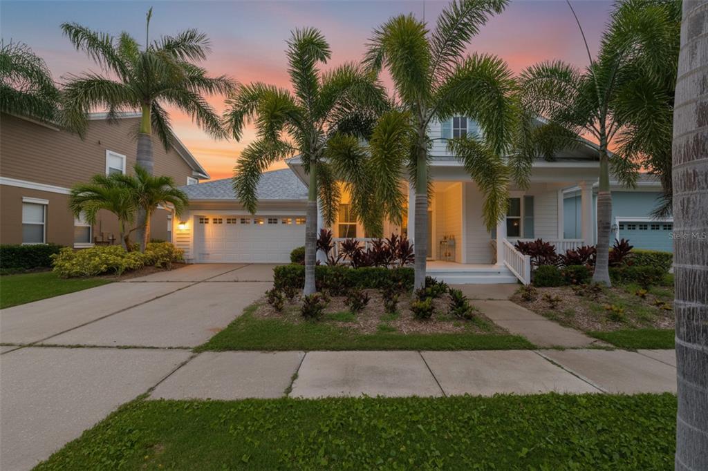A single-story house with a white exterior, a two-car garage, and palm trees at sunset — 404 ISLEBAY DRIVE, APOLLO BEACH, FL