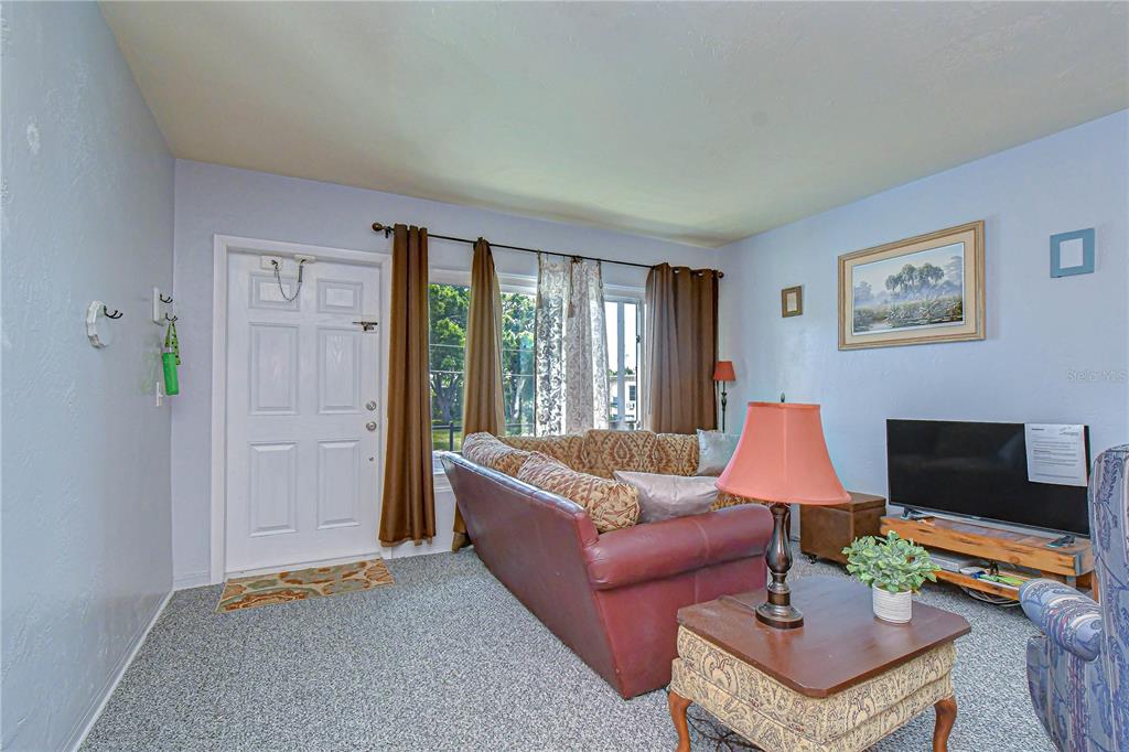 A living room features a red sofa, a television on a wooden stand, and carpeted flooring — 4022 57TH STREET N UNIT 260, KENNETH CITY, FL