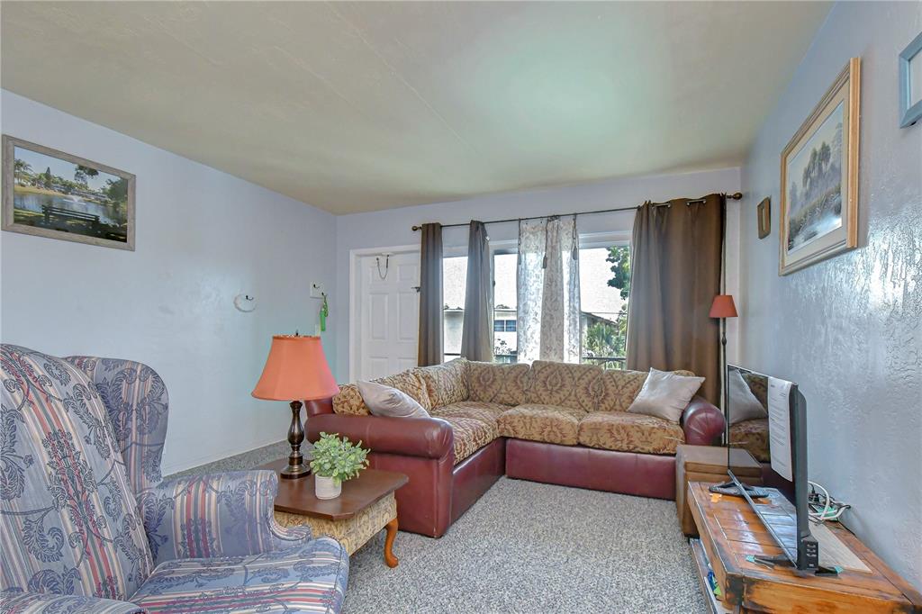 A living room features a patterned armchair, a sectional sofa, and a television on a stand — 4022 57TH STREET N UNIT 260, KENNETH CITY, FL