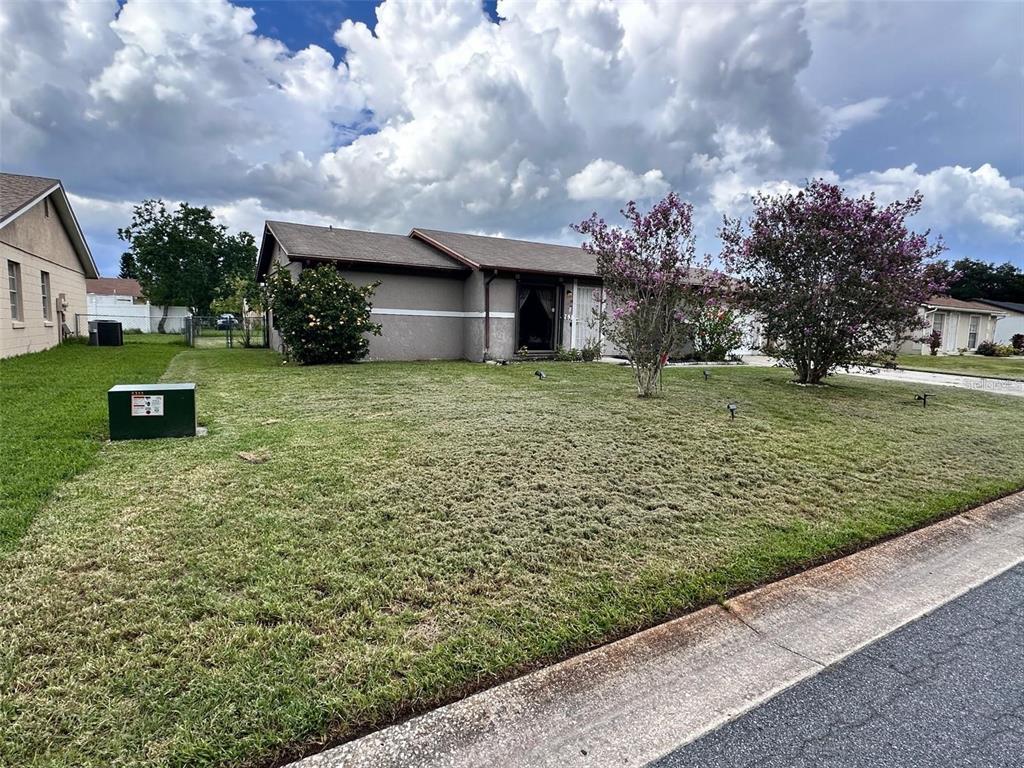 A single-story house with a gray stucco exterior, a brown roof, and two flowering trees — 263 LA PAZ DRIVE, KISSIMMEE, FL