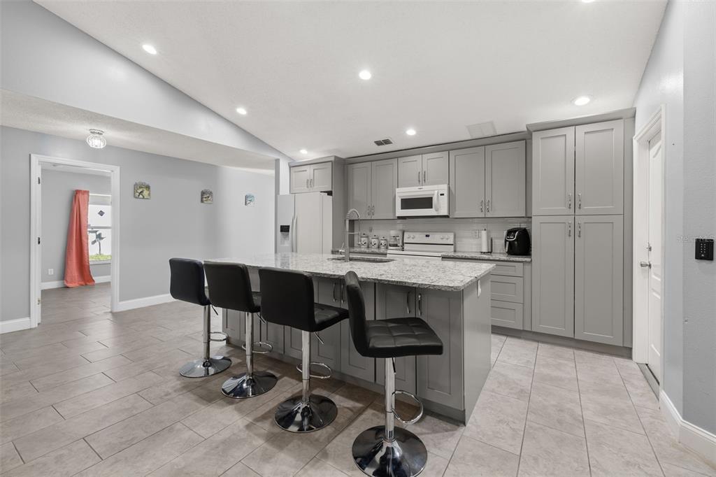 A kitchen with gray cabinets, granite countertops, a central island with bar stools, and tile flooring — 60 ANDORA COURT, KISSIMMEE, FL