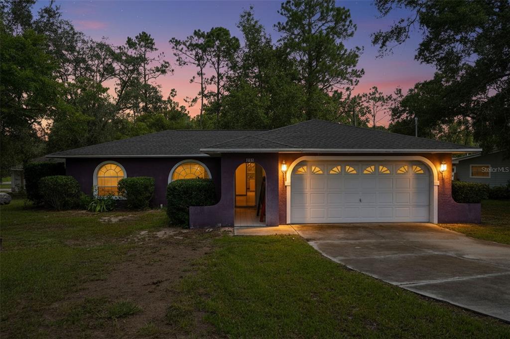 A purple single-story house with a two-car garage and arched windows at dusk — 1325 W SORRENTO DRIVE, CITRUS SPRINGS, FL