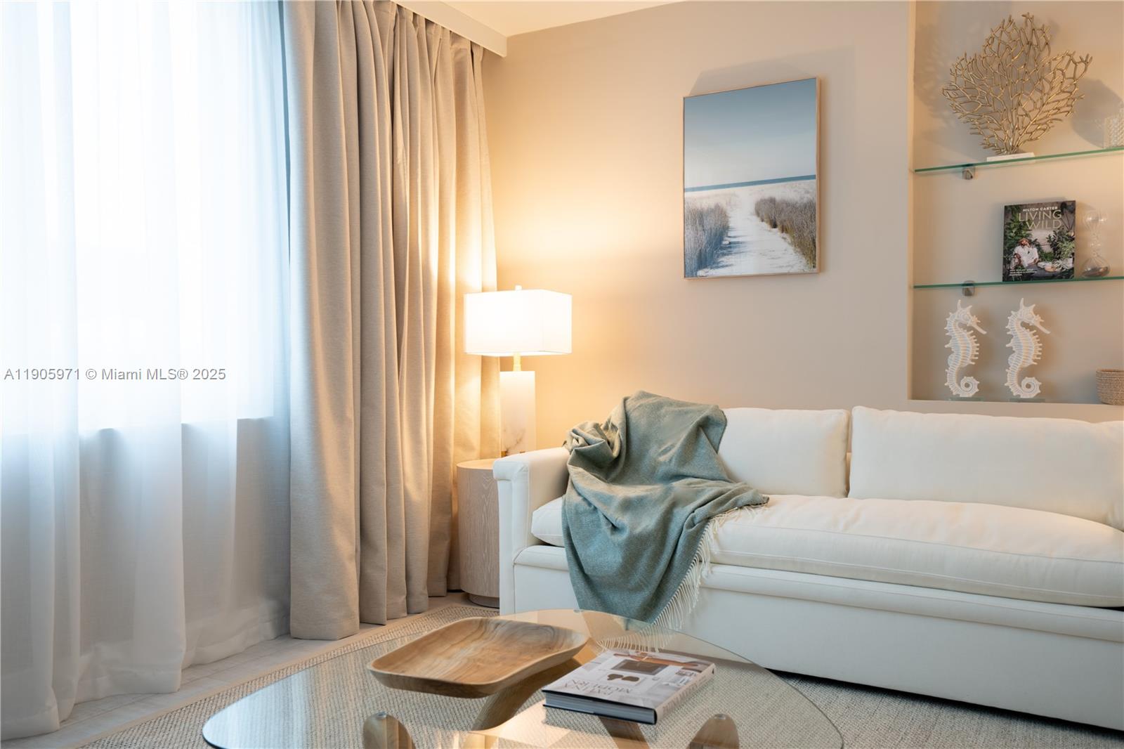 A white sofa with a green throw blanket sits in a living room with curtains — 2301 Collins Ave # 836, Miami Beach FL 33139, MIAMI BEACH, FL