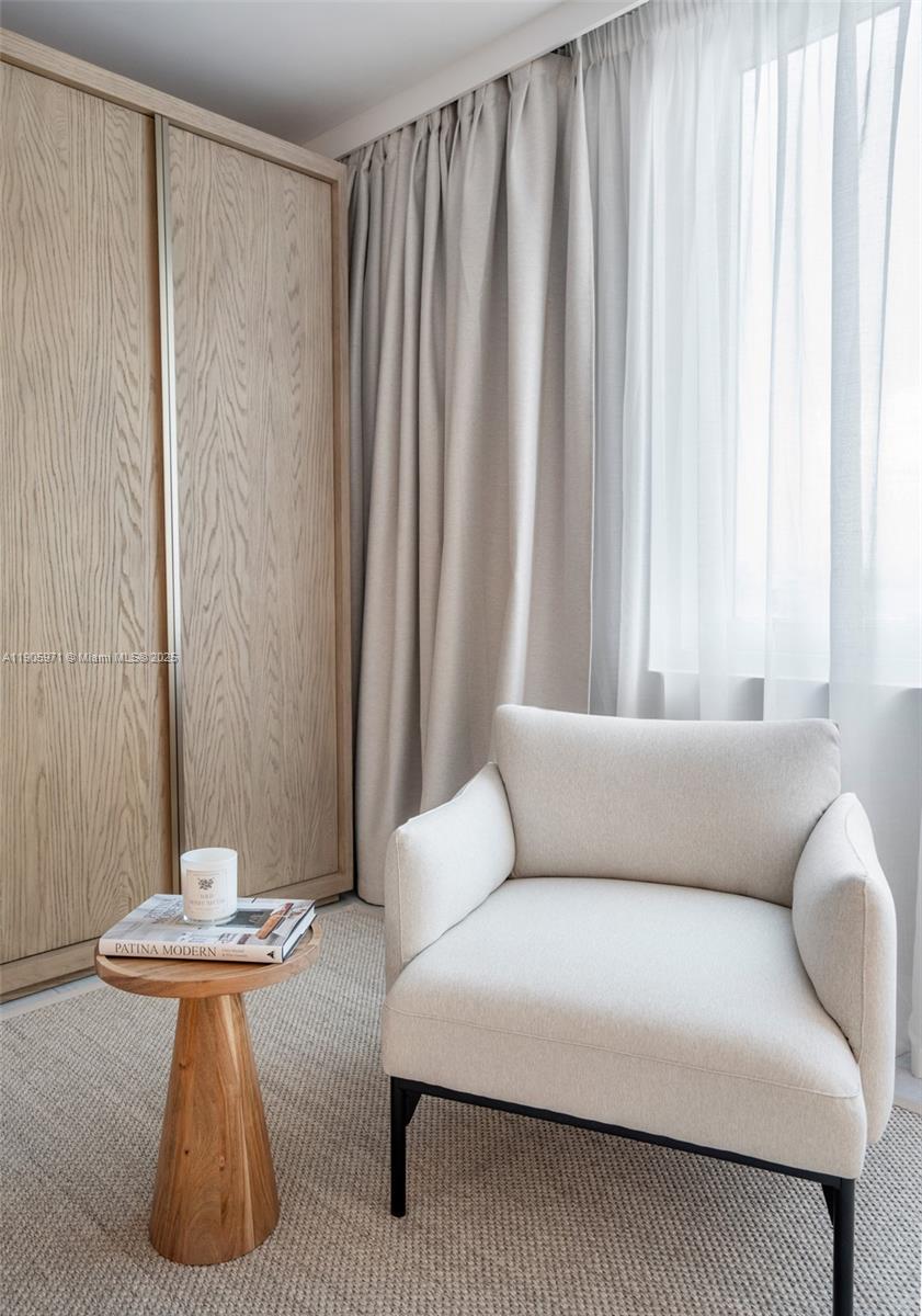 A light-colored armchair sits on a rug next to a wooden side table and wardrobe — 2301 Collins Ave # 836, Miami Beach FL 33139, MIAMI BEACH, FL