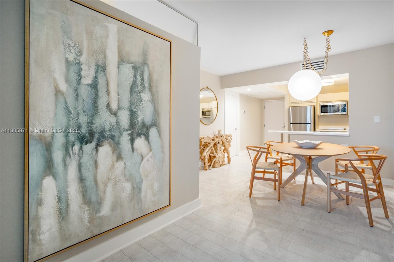 A dining area features a round wooden table, light-colored wood chairs, and a large abstract painting — 2301 Collins Ave # 836, Miami Beach FL 33139, MIAMI BEACH, FL