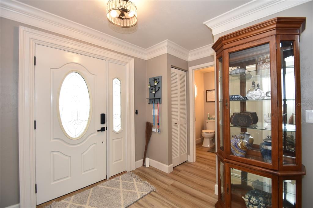 An entryway features a white front door, wood-look flooring, a glass display cabinet, and crown molding — 1 BEDFORD DRIVE, PALM COAST, FL