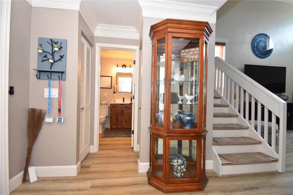 A wooden curio cabinet stands in a hallway next to a staircase and a bathroom — 1 BEDFORD DRIVE, PALM COAST, FL