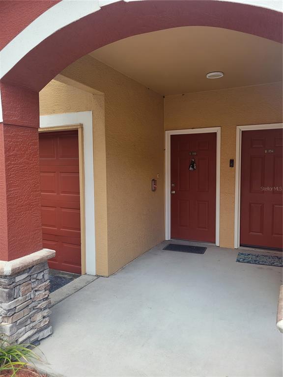 An exterior view of a covered entryway with two red doors and a garage door — 2139 CHIANTI PLACE UNIT 5-0153, PALM HARBOR, FL