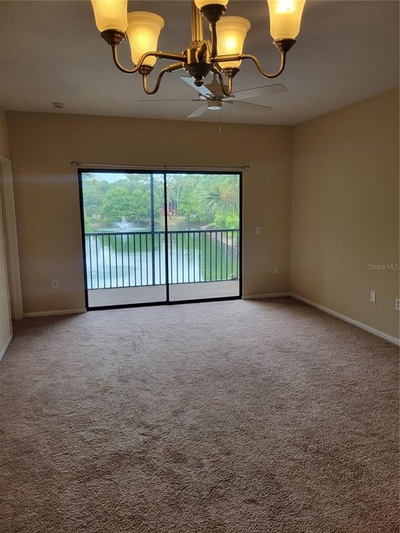 A carpeted bedroom features a ceiling fan, a chandelier, and a sliding door to a balcony — 2139 CHIANTI PLACE UNIT 5-0153, PALM HARBOR, FL