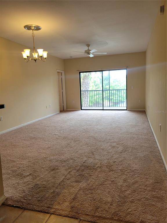 A carpeted living room features a ceiling fan, a chandelier, and sliding glass balcony doors — 2139 CHIANTI PLACE UNIT 5-0153, PALM HARBOR, FL
