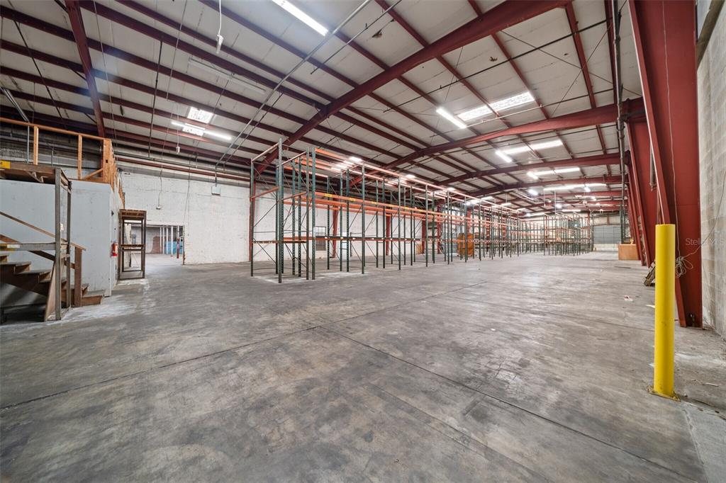 A large warehouse interior features concrete floors, exposed steel beams, and rows of metal shelving — 506 SE 3RD AVENUE, OCALA, FL