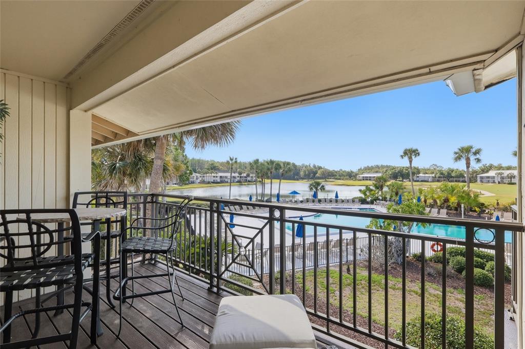 A balcony with outdoor furniture overlooks a swimming pool, a lake, and palm trees — 29130 BAY HOLLOW DRIVE UNIT 3312, WESLEY CHAPEL, FL