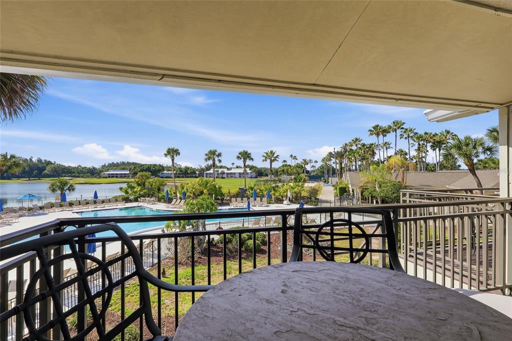 A balcony with a stone table overlooks a swimming pool, a lake, and palm trees — 29130 BAY HOLLOW DRIVE UNIT 3312, WESLEY CHAPEL, FL