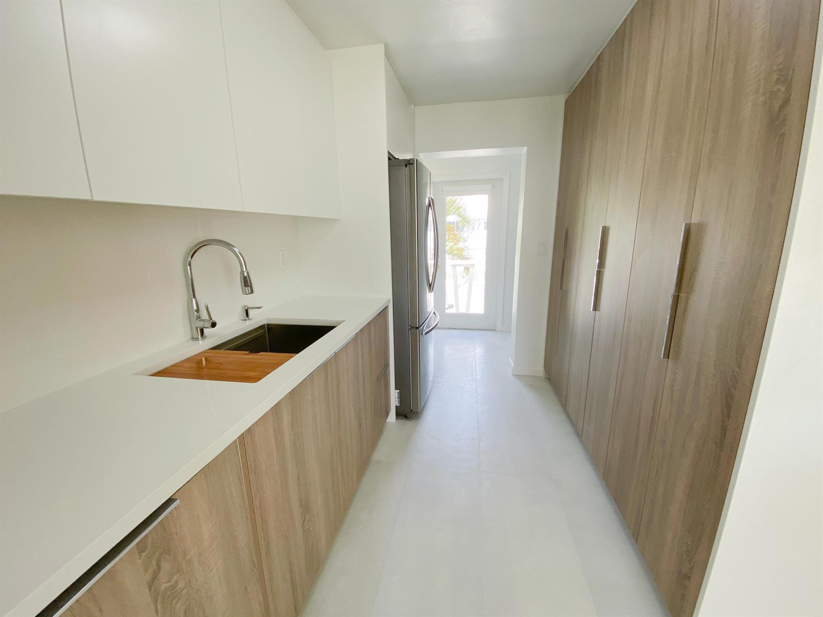 A galley kitchen features white upper cabinets, wood-grain lower cabinets, and a stainless steel refrigerator — 2755 NE 28th Avenue # C1, Lighthouse Point FL 33064, LIGHTHOUSE POINT, FL