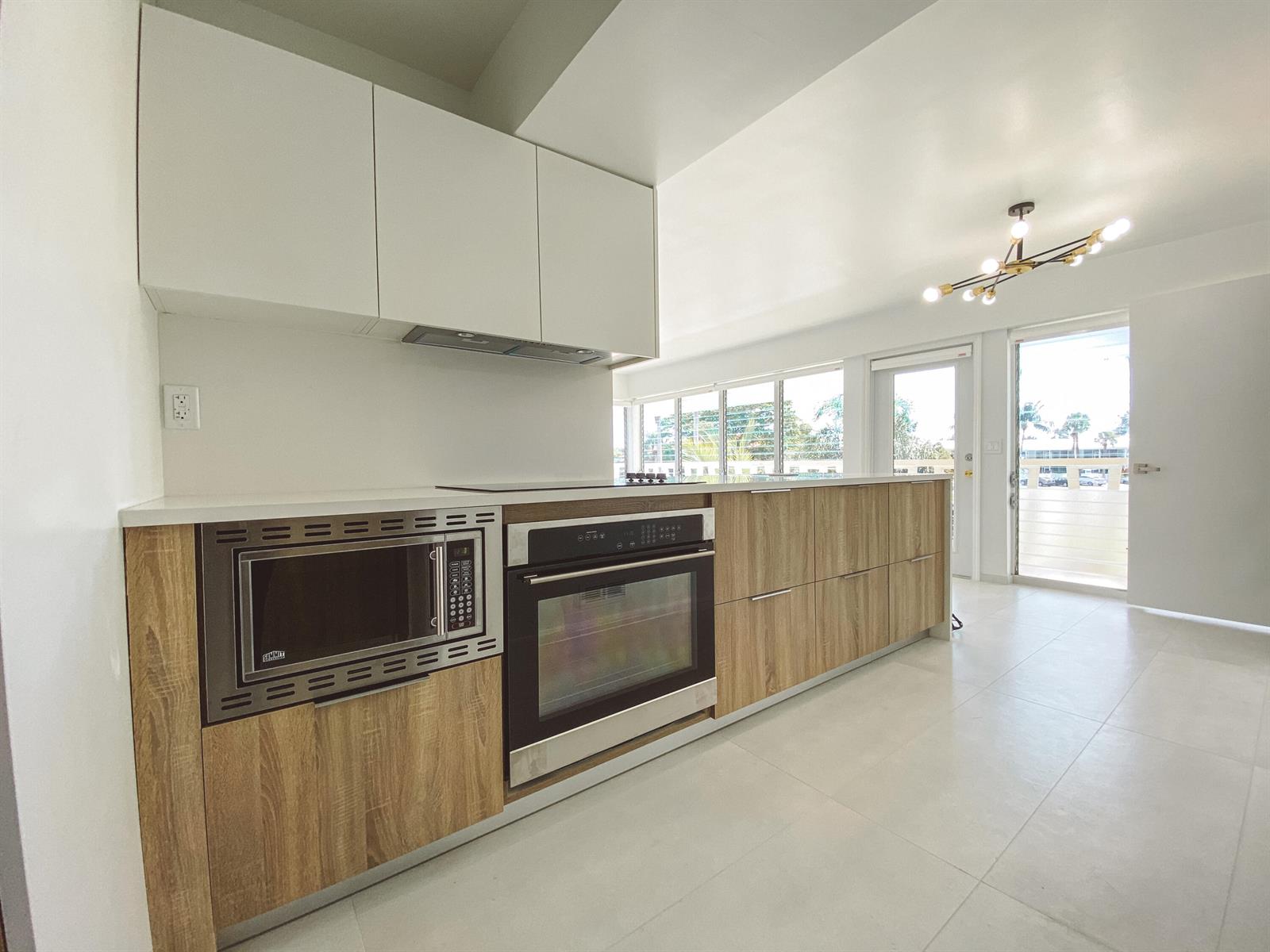 A modern kitchen features wood-grain lower cabinets, white upper cabinets, stainless steel appliances, and tile flooring — 2755 NE 28th Avenue # C1, Lighthouse Point FL 33064, LIGHTHOUSE POINT, FL