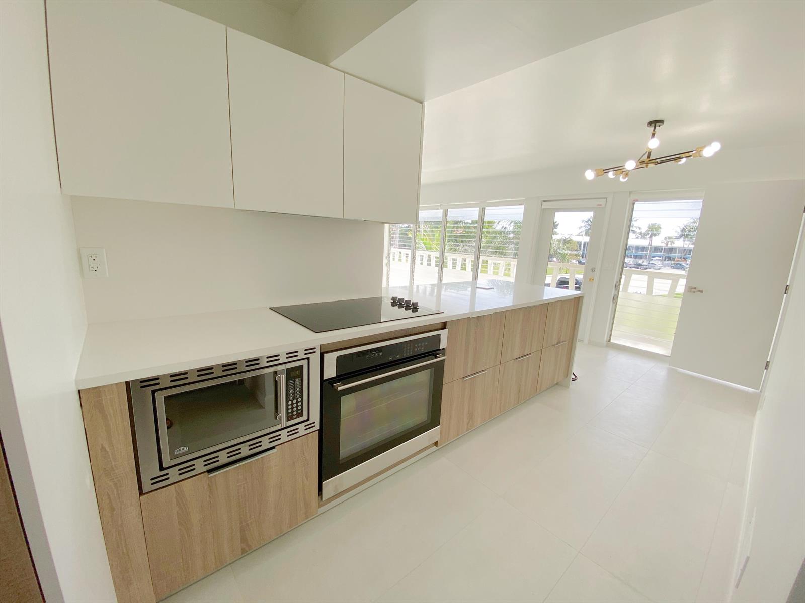 A modern kitchen features white upper cabinets, wood-grain lower cabinets, stainless steel appliances, and tile flooring — 2755 NE 28th Avenue # C1, Lighthouse Point FL 33064, LIGHTHOUSE POINT, FL