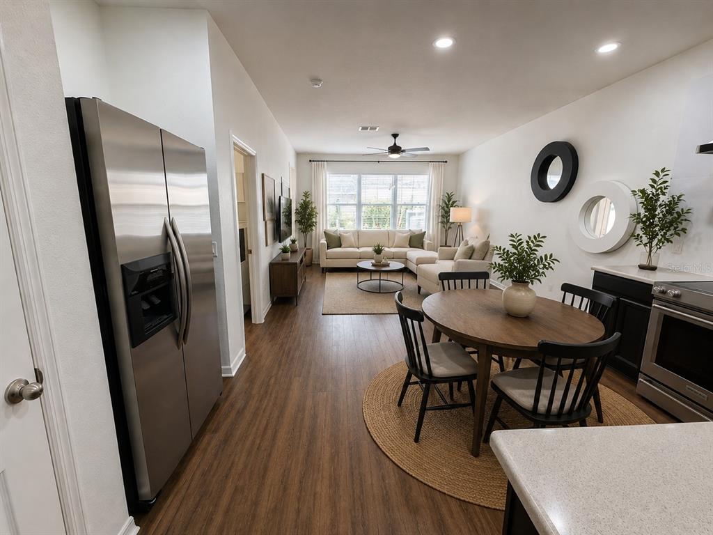 An open-concept living and dining area features stainless steel appliances, wood flooring, and neutral furniture — 12210 LANGSTAFF DRIVE, WINDERMERE, FL