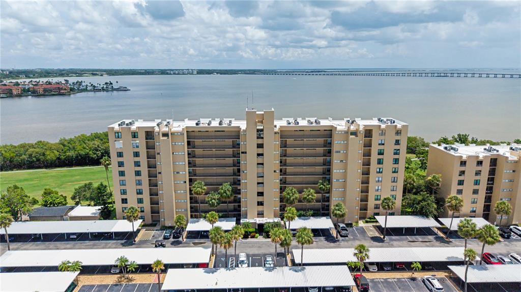An aerial view shows a multi-story apartment building with covered parking lots near a bay — 2618 COVE CAY DRIVE UNIT 109, CLEARWATER, FL