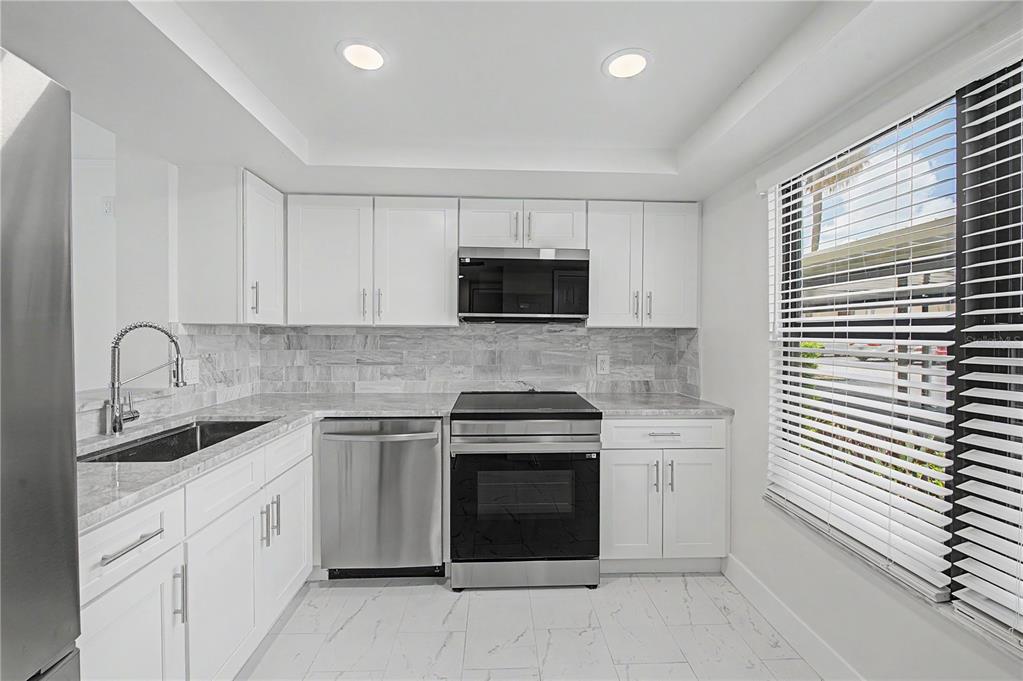 A modern kitchen features white cabinets, stainless steel appliances, marble-style countertops, and tile flooring — 2618 COVE CAY DRIVE UNIT 109, CLEARWATER, FL