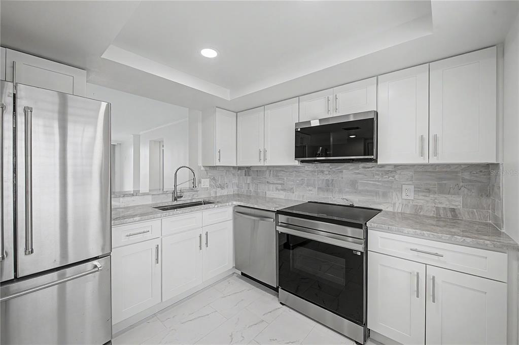 A modern kitchen features white cabinets, stainless steel appliances, and gray marble-patterned countertops and backsplash — 2618 COVE CAY DRIVE UNIT 109, CLEARWATER, FL