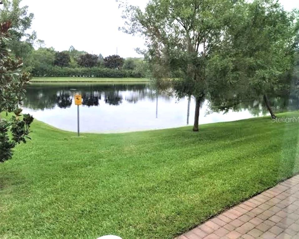 A grassy lawn slopes down toward a calm pond with a warning sign — 3603 SANCTUARY DRIVE, ST CLOUD, FL