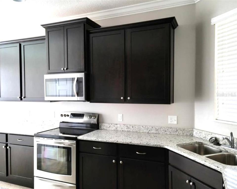 A kitchen features dark wood cabinets, granite countertops, and stainless steel appliances — 3603 SANCTUARY DRIVE, ST CLOUD, FL