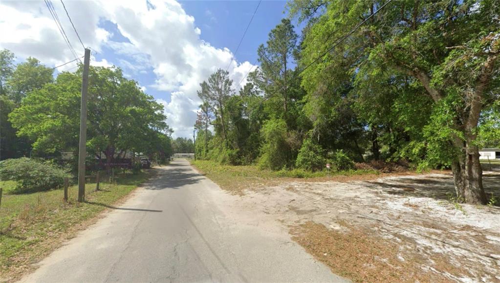 A paved road runs between a wooded lot and a grassy area with utility poles — TBD SE 129 CT, SILVER SPRINGS, FL