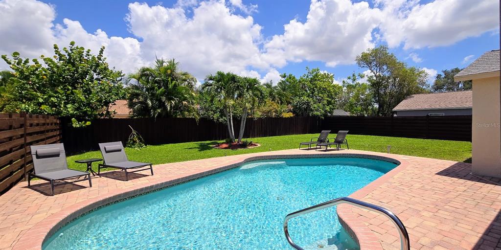 A backyard features a swimming pool, brick patio, lounge chairs, and a wooden privacy fence — 3803 EASTON STREET, SARASOTA, FL
