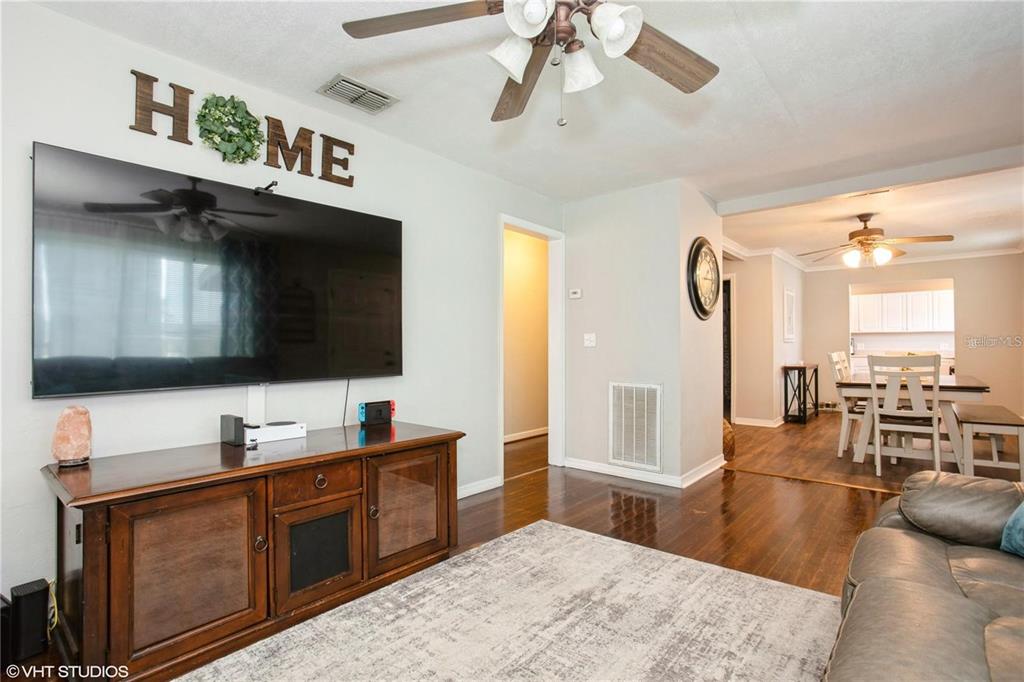 A living room with a large wall-mounted television, wooden media console, and an adjacent dining area — 1813 5TH STREET W, PALMETTO, FL