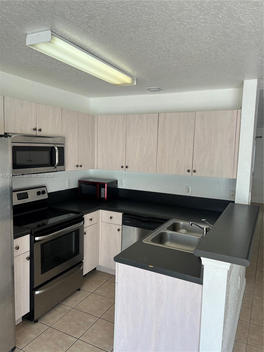 A kitchen features light wood cabinets, black countertops, stainless steel appliances, and tiled flooring — 183 Hidden Ct Rd # 33, Hollywood FL 33023, HOLLYWOOD, FL