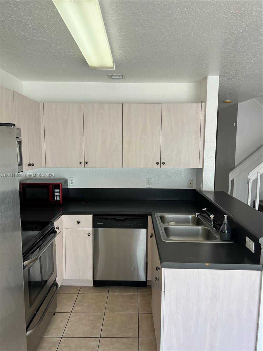 A kitchen features light wood cabinets, black countertops, stainless steel appliances, and tile flooring — 183 Hidden Ct Rd # 33, Hollywood FL 33023, HOLLYWOOD, FL