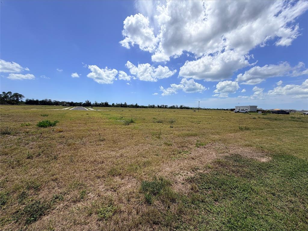 A wide, grassy, undeveloped lot under a bright blue sky with scattered clouds — 254 HOLLY BANK AVENUE, NOKOMIS, FL