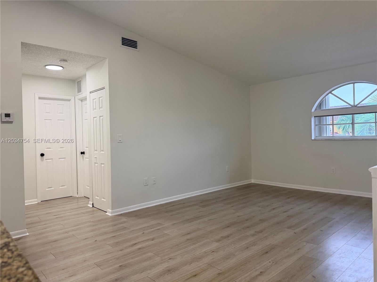 An empty room features light wood-look flooring, white walls, and an arched window — 7730 W 34th Ln # 202, Hialeah FL 33018, HIALEAH, FL